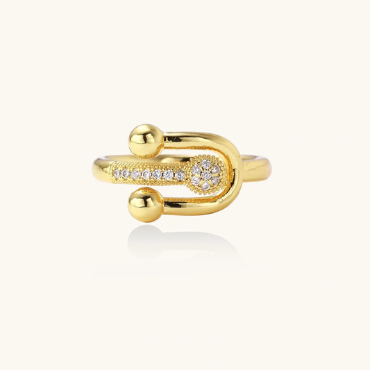 Gold-plated brass ring with safety pin design featuring pavé cubic zirconia stones and dual sphere ends