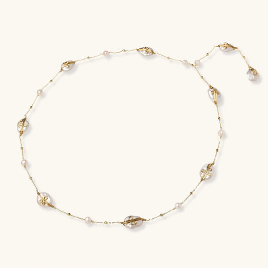 Long gold chain necklace with baroque pearls wrapped in leaf designs and small freshwater pearls spaced along the strand
