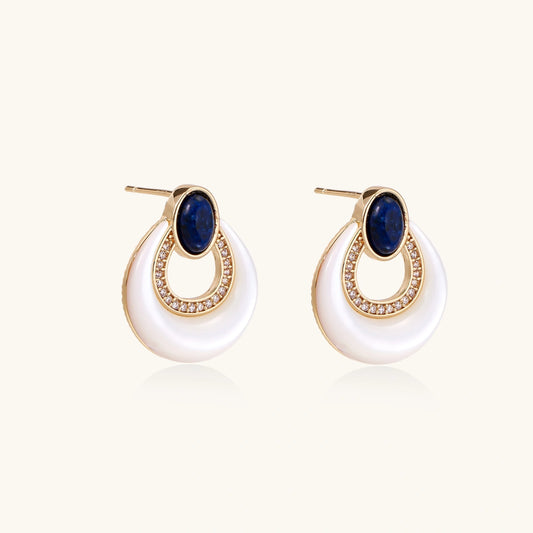 Gold drop earrings with oval lapis lazuli, crystal-paved frame, and iridescent mother-of-pearl teardrop on cream background