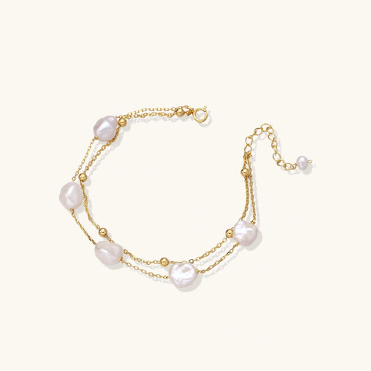 Double-strand gold bracelet with irregular baroque pearls and smooth freshwater pearls on cream background.