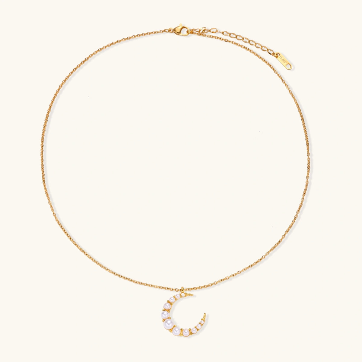 Gold crescent moon pendant with graduated white pearls on delicate chain against cream background