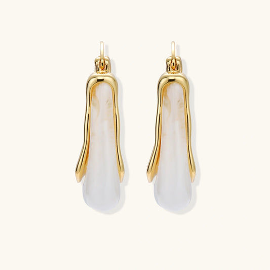 Sculptural gold-plated hoop earrings with flowing curved design and lever-back closure on cream background.